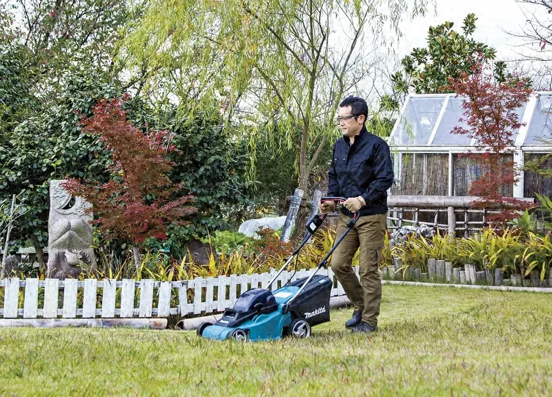 Lawn care worker pushing a mower across a front yard beside a white picket fence